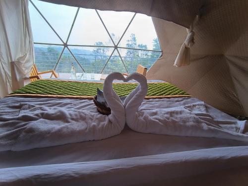 two swans making a heart on a bed with a window at L.T NATURE GLAMPS in Kodaikānāl