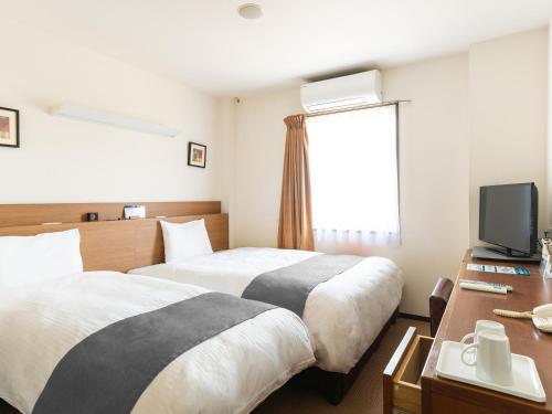 a hotel room with two beds and a television at Vessel Hotel Higashi Hiroshima in Higashihiroshima