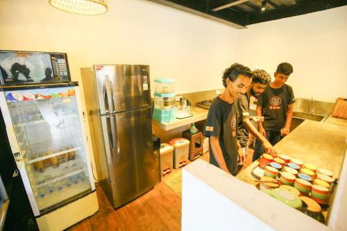 three men standing in a kitchen with a refrigerator at Hangover Hostels Ella in Ella
