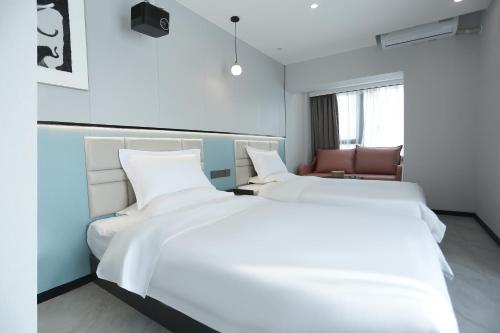 two white beds in a room with a chair at Yunbo Youth Hostel Ürümqi in Ürümqi