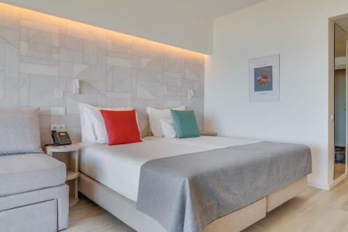 a bedroom with a large white bed with colorful pillows at Pestana Blue Alvor Beach - All Inclusive Hotel in Alvor