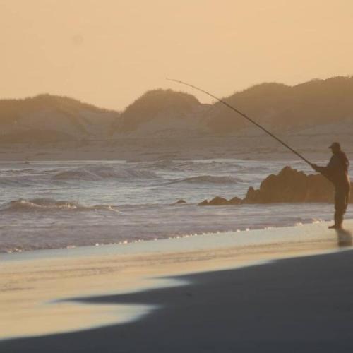 a man fishing on the beach at sunset at Beach Walk by Salted Fynbos Staying in Pearly Beach
