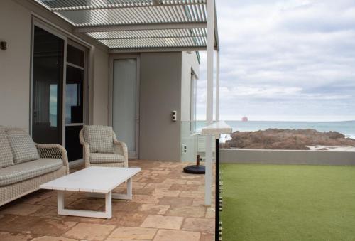 a patio with a table and chairs and a view of the ocean at Bokkombaai in Bloubergstrand