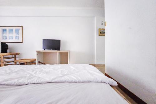 1 dormitorio con 1 cama blanca y TV en Kondominium Carita Wawan Mitra RedDoorz, en Pandegelang