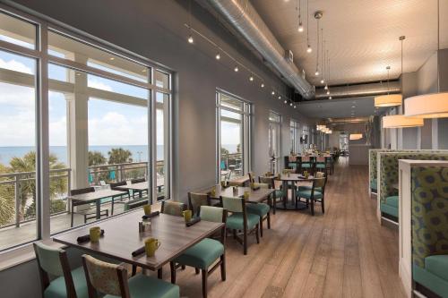 un restaurante con mesas, sillas y ventanas grandes en The Ellie Beach Resort Myrtle Beach, Tapestry By Hilton en Myrtle Beach