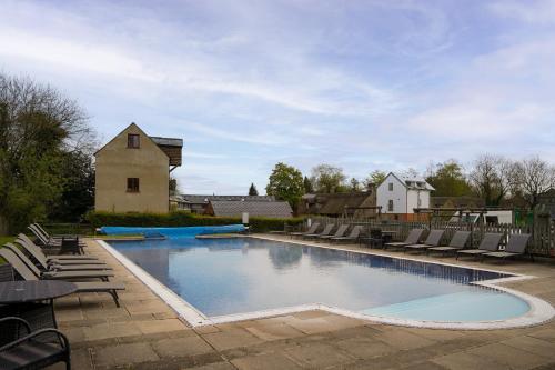 a large swimming pool with chairs and a house at Toad Hall Pet-Friendly Family Stay, Lake Access in Somerford Keynes
