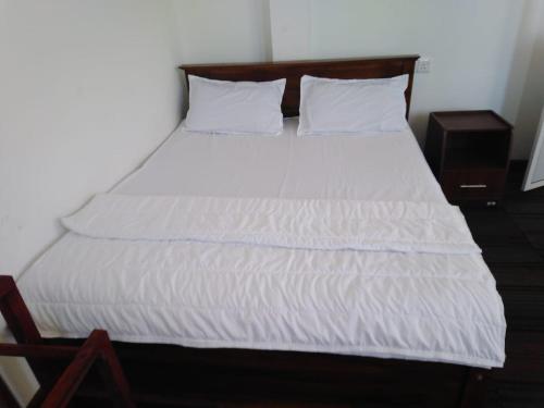 a bed with white sheets and a wooden headboard at Frosty Heaven Guest House in Nuwara Eliya