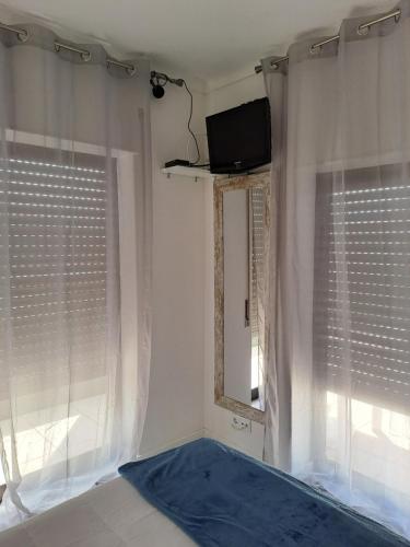 a room with a tv and two windows with curtains at apartamento perto do Santuário in Fátima