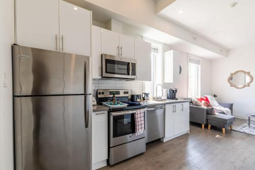 La cuisine est équipée de placards blancs et d'un réfrigérateur en acier inoxydable. dans l'établissement Spacious 2BR Apartment - Minutes to Leslieville, à Toronto
