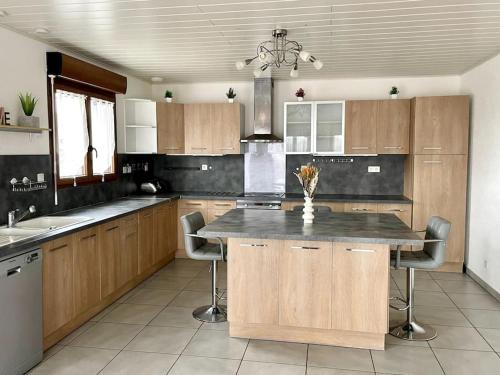 une cuisine avec des placards en bois et un îlot de cuisine avec des chaises dans l'établissement Maison Les Tilleuls, à Les Pontets