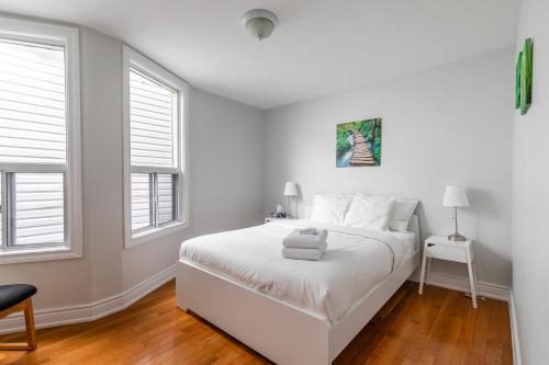 a white bedroom with a bed and two windows at Pet-Friendly 3BR Apartment - Ossington Ave in Toronto