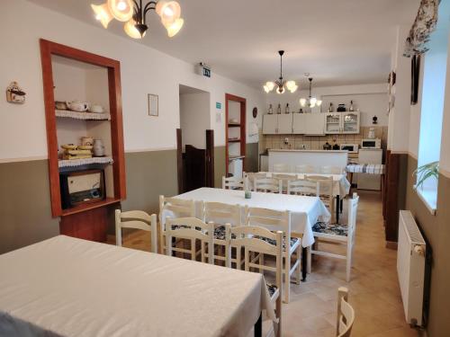 uma sala de jantar com mesas e cadeiras brancas e uma cozinha em Ódon Panzió em Bükkszentkereszt