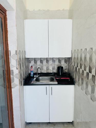uma cozinha com armários brancos e um lavatório em AM a shared room em Doha