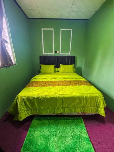 a bed in a green room with a yellow blanket at Green Savannah Homestay Syariah in Dieng