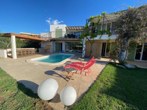 une maison avec une piscine et deux chaises rouges dans l'établissement Villa bord de mer avec piscine 200 métres plage, à Zonza