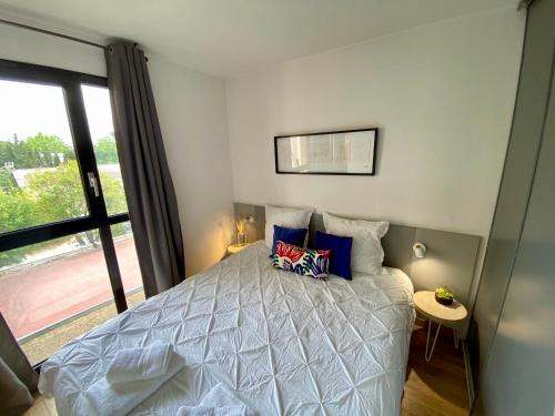 ein Schlafzimmer mit einem Bett mit blauen Kissen und einem Fenster in der Unterkunft Ma place au sud Aix Parking in Aix-en-Provence