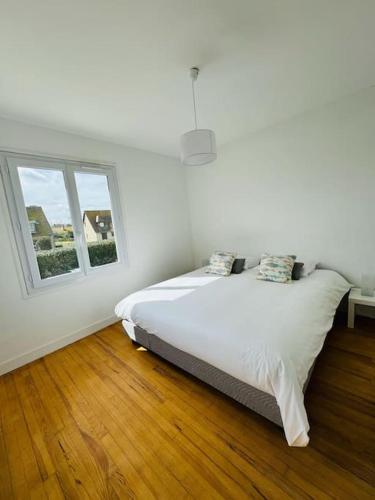 a white bedroom with a bed and two windows at Demeure rénovée front de mer in Courseulles-sur-Mer