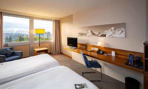 a hotel room with two beds and a desk with a computer at Mövenpick Hotel Geneva in Geneva