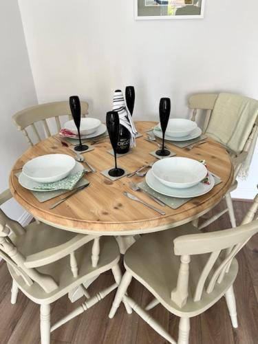 a wooden table with plates and wine glasses on it at Tranquil 2-Bed Bungalow Near to Southwold in Wrentham