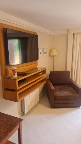 a living room with a flat screen tv and a chair at Flat em Gramado in Gramado