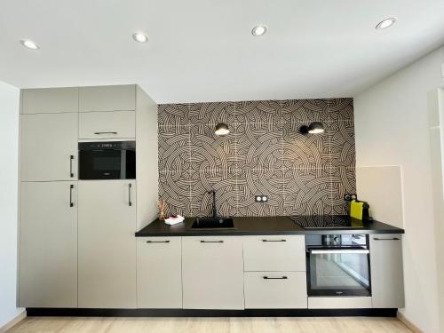 une cuisine avec des placards blancs et un mur à motifs dans l'établissement PGH N12 - Thalasso & Plage à 2 pas, Parking Privé, à La Grande Motte