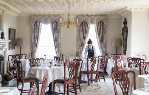 kobieta stojąca w pokoju ze stołami i krzesłami w obiekcie Chilston Park Hotel w mieście Lenham