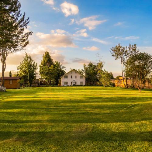 a large grass field with a white house in the distance at Hosteria Airport Garden in Tababela