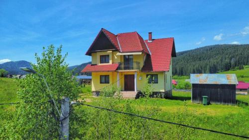 a yellow house with a red roof on a green field at Casa de vacanta in Borsec