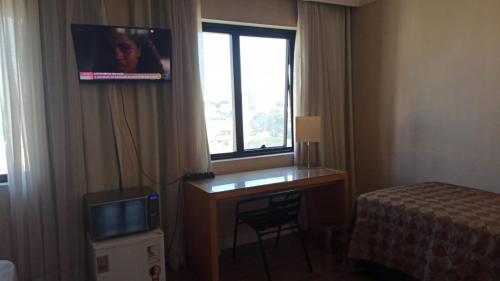 a hotel room with a desk and a tv on the wall at Slaviero1411 in Guarulhos