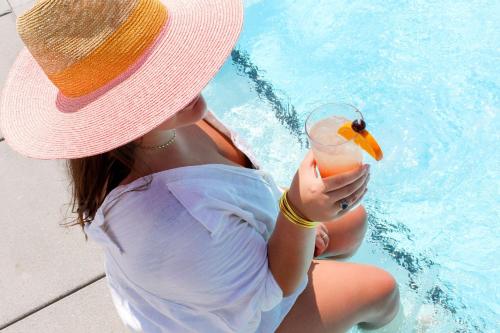 a woman in a hat holding a drink next to a pool at Hotel Effie Sandestin Resort, Autograph Collection in Destin