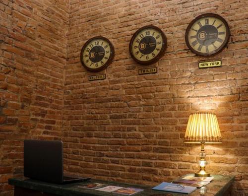 two clocks on a brick wall with a lamp and a laptop at Belona Hotel in Kutaisi