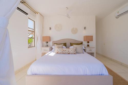 a white bedroom with a large white bed with pillows at Kuza The Palm Villas at Vipingo in Kilifi