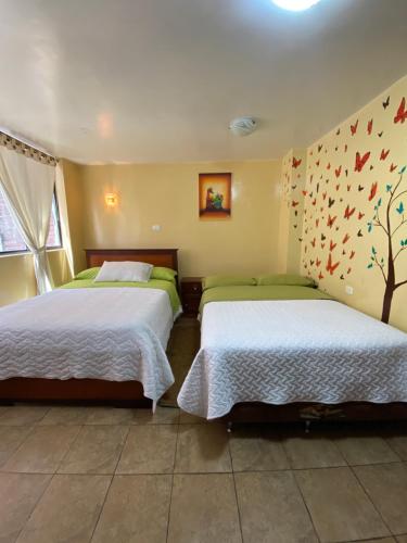a bedroom with two beds and a tree on the wall at Hostal El Oro in Baños
