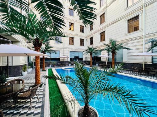uma piscina de hotel com uma palmeira em frente a um edifício em Medina Hotel Samarkand em Samarkand