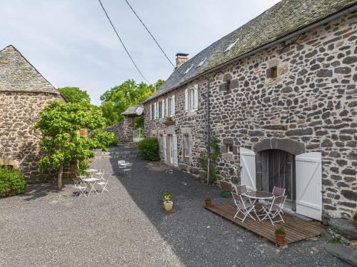 a stone house with chairs and a table in a courtyard at LA LONGÈRE - Chambres et table d'hôtes in Alpuech