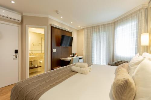 a bedroom with a large white bed and a bathroom at Hotel Jardins da Colina in Nova Petrópolis