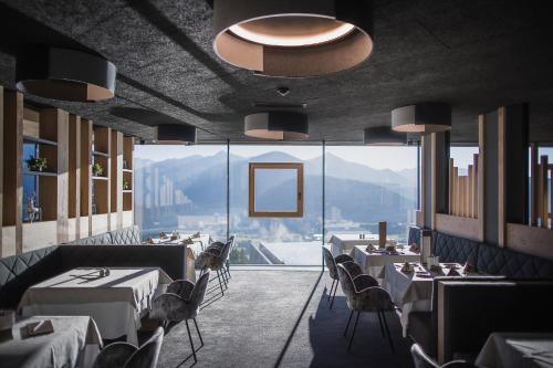 restauracja ze stołami i krzesłami oraz dużym oknem w obiekcie Alpin Panorama Hotel Hubertus w mieście Valdaora