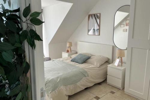 a white bedroom with a bed and a plant at Cosy apartment with large terrace near the beach in Barneville-Carteret