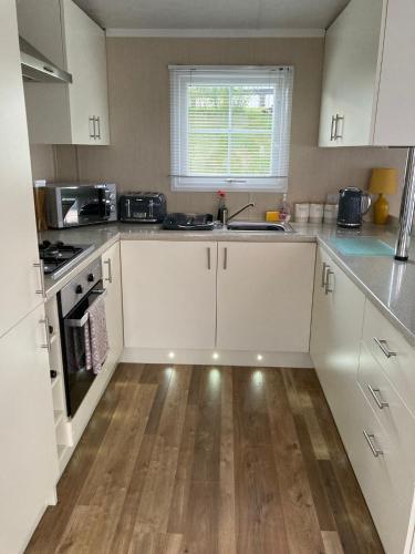 a kitchen with white cabinets and a wooden floor at Lakes edge view in Millom