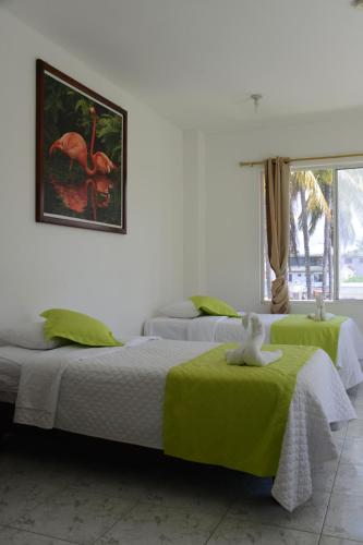 a bedroom with two beds with green sheets and a picture at Hostal Las Fragatas in Puerto Villamil