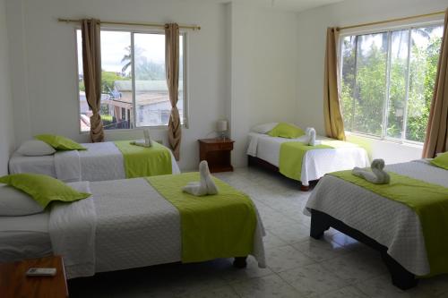 a room with three beds with green sheets and windows at Hostal Las Fragatas in Puerto Villamil