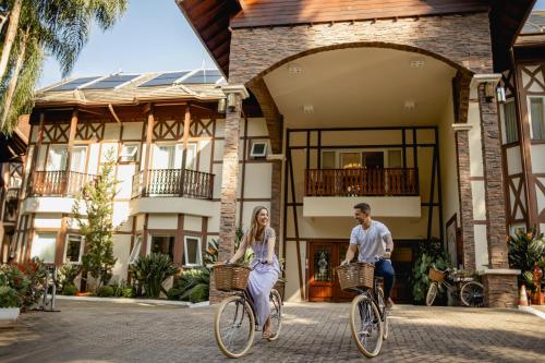 Ein Mann und eine Frau, die vor einem Haus Fahrrad fährt in der Unterkunft Hotel Jardins da Colina in Nova Petrópolis