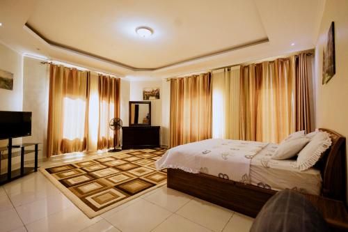 ADRIEL HOMES WOODLAND CENTEr في كيغالي: غرفة نوم بسرير وتلفزيون وستائر