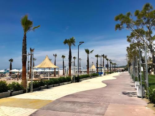 a sidewalk next to a beach with palm trees and umbrellas at Delight Apartments in Golem