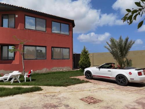 un coche blanco estacionado frente a una casa roja en Villa Mostafa Sadek, Swimming pool, Tennis & Squash - Borg ElArab Airport Alexandria en Borg El Arab