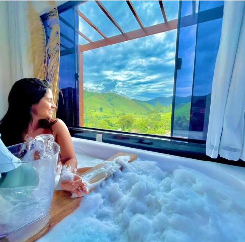 a woman sitting in a bath tub with a window at Chalés La Vista - Visconde de Mauá in Visconde De Maua