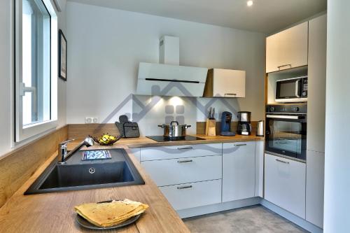 une cuisine avec des armoires blanches et un évier dans l'établissement LocaLise - M1 - Bain de mer - Maison entièrement rénové avec jardin clos - Wifi inclus - Draps inclus - Animaux bienvenus, à Tréffiagat
