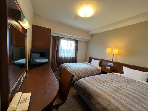 弘前市にあるホテルルートイン弘前城東のベッド2台とデスクが備わるホテルルームです。