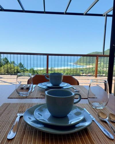 a table with plates and cups and utensils on a balcony at Casa Yogui Brasil in Garopaba