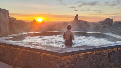 een persoon die in een hot tub zit en naar de zonsondergang kijkt bij Miðhraun - Lava resort in Midhraun